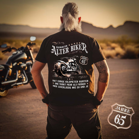 Ein Biker mit einem T-Shirt zum Geburtstag für Motorradfahrer von Wingbikers mit dem Aufdruck, Alter Biker - 65 Jahre - Einige Kilometer runter, trinkt mehr - aber zuverlässig wie eh und je - mit Back Print, in schwarz.