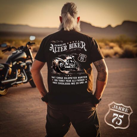 Ein Biker mit einem T-Shirt zum Geburtstag für Motorradfahrer von Wingbikers mit dem Aufdruck, Alter Biker - 75 Jahre - Einige Kilometer runter, trinkt mehr - aber zuverlässig wie eh und je - mit Back Print, in schwarz.