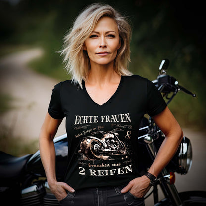 Eine Motorradfahrerin mit einem T-Shirt mit V-Ausschnitt von Wingbikers mit dem Aufdruck, Echte Frauen brauchen nur zwei Reifen, in schwarz.