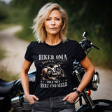 Eine Frau mit einem T-Shirt für Motorradfahrerinnen von Wingbikers mit dem Aufdruck, Biker Oma - Benzin im Blut - Oma mit Herz und Seele, leger geschnitten, in schwarz.