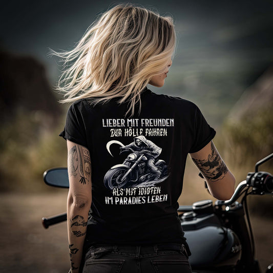 Eine Bikerin mit einem T-Shirt für Motorradfahrerinnen von Wingbikers mit dem Aufdruck, Lieber mit Freunden zur Hölle fahren, als mit Idioten im Paradies leben, leger geschnitten, als Back Print, in schwarz.
