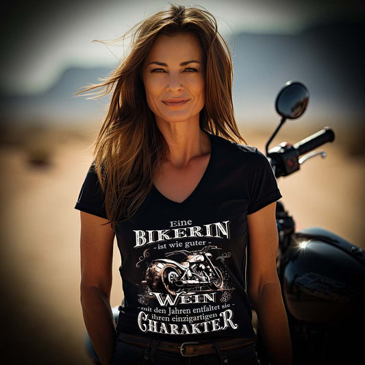 Eine Bikerin mit einem T-Shirt mit V-Ausschnitt für Motorradfahrerinnen von Wingbikers mit dem Aufdruck, Eine Bikerin ist wie guter Wein - mit den Jahren entfaltet sie ihren einzigartigen Charakter - in schwarz.