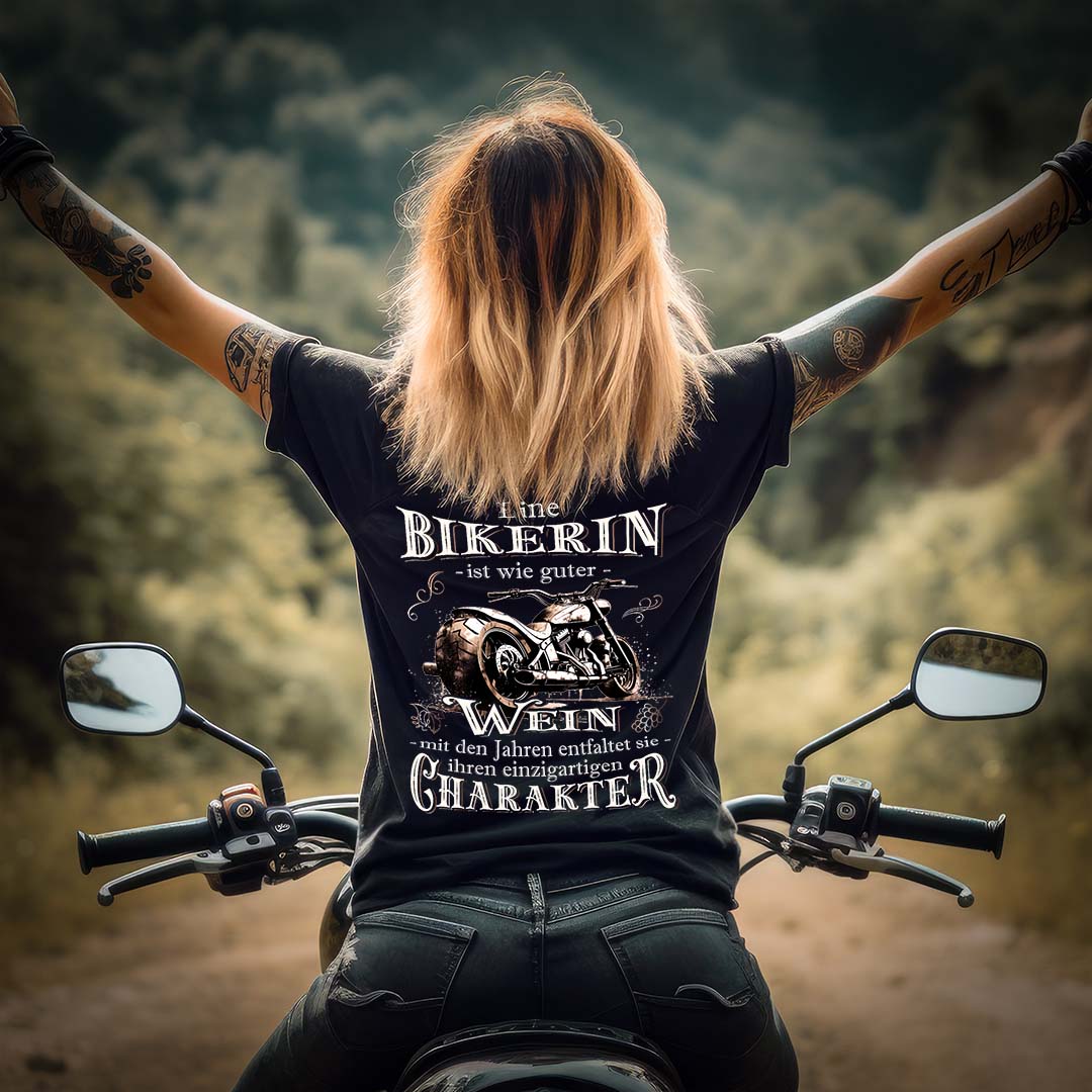 Eine Bikerin mit einem T-Shirt für Motorradfahrerinnen von Wingbikers mit dem Aufdruck, Eine Bikerin ist wie guter Wein - mit den Jahren entfaltet sie ihren einzigartigen Charakter - mit Back Print, in schwarz.