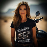 Eine Bikerin mit einem Geburtstags-T-Shirt für Motorradfahrerinnen von Wingbikers mit dem Aufdruck, Alte Bikerin - 55 Jahre - Einige Kilometer Runter - Doch elegant wie eh und je - in schwarz.