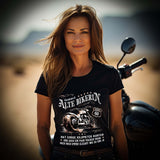 Eine Bikerin mit einem Geburtstags-T-Shirt für Motorradfahrerinnen von Wingbikers mit dem Aufdruck, Alte Bikerin - 60 Jahre - Einige Kilometer Runter - Doch elegant wie eh und je - in schwarz.