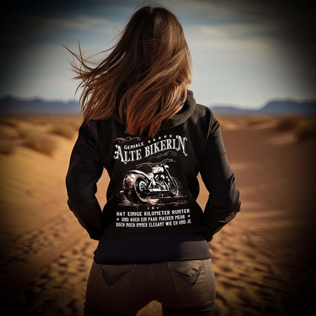 Eine Bikerin mit einem Hoodie für Motorradfahrerinnen von Wingbikers mit dem Aufdruck, Alte Bikerin - Einige Kilometer Runter - Doch elegant wie eh und je - mit Back Print, in schwarz.