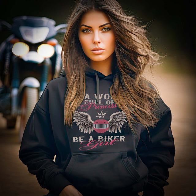 Ein Frau mit einem Damen Hoodie für Motorradfahrerinnen von Wingbikers mit dem Aufdruck, In A World Full Of Princesses - Be A Biker Girl, in schwarz.