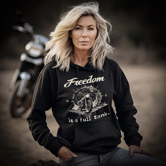 Eine Bikerin mit einem Damen Hoodie für Motorradfahrerinnen von Wingbikers mit dem Aufdruck, Freedom Is A Full Tank - Freiheit ist ein voller Tank - mit einem Retro Vintage klassischem Motorrad, in schwarz.