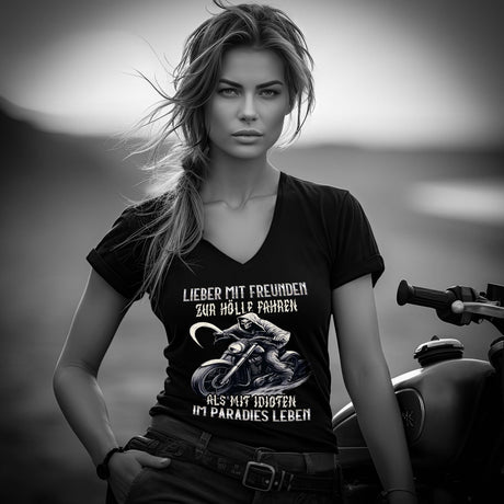 Eine Motorradfahrerin mit einem T-Shirt mit V-Ausschnitt von Wingbikers mit dem Aufdruck, Lieber mit Freunden zur Hölle fahren, als mit Idioten im Paradies leben, in schwarz.