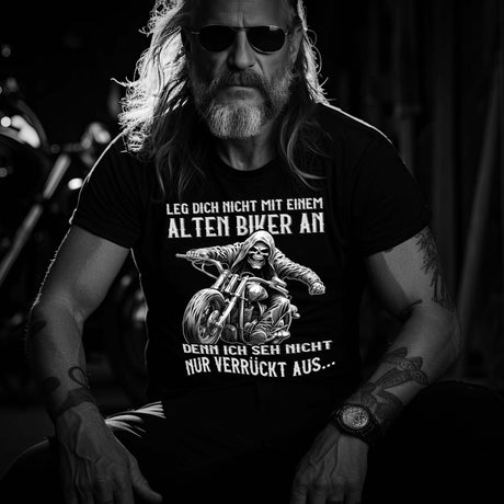 Ein Biker mit einem T-Shirt für Motorradfahrer von Wingbikers mit dem Aufdruck, Leg dich nicht mit einem alten Biker an, denn ich seh nicht nur verrückt aus - in schwarz.