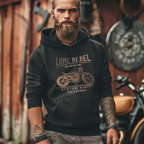 Ein Biker mit einem Hoodie für Motorradfahrer von Wingbikers mit dem Aufdruck, Lone Rebel - Shaped by time - Custom Biker, in schwarz.