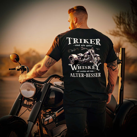 Ein Mann mit einem T-Shirt für Trike Fahrer von Wingbikers mit dem Aufdruck, Triker sind wie guter Whiskey - Wir werden mit dem Alter besser, als Back Print, in schwarz.