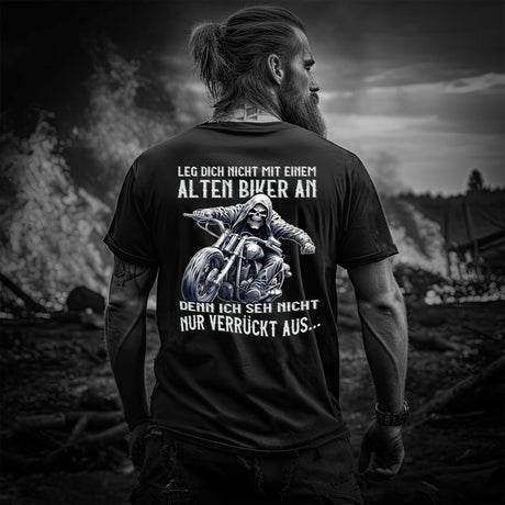 Ein Biker mit einem T-Shirt für Motorradfahrer von Wingbikers mit dem Aufdruck, Leg dich nicht mit einem alten Biker an, denn ich seh nicht nur verrückt aus, als Back Print - in schwarz.