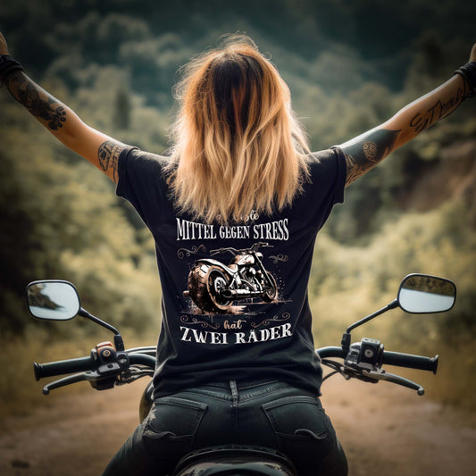 Eine Motorradfahrerin mit einem T-Shirt von Wingbikers mit dem Aufdruck auf dem Rücken, Das beste Mittel gegen Stress hat 2 Räder - mit Back Print, leger geschnitten, in schwarz.
