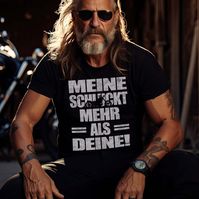 Ein Biker mit einem T-Shirt für Motorradfahrer von Wingbikers mit dem Aufdruck, Meine schluckt mehr als deine! mit einem Motorrad, in schwarz.