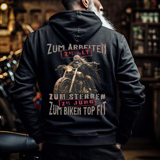 Ein Biker mit einer Reißverschluss-Jacke für Motorradfahrer von Wingbikers mit dem Aufdruck, Zum Arbeiten zu alt, zum Sterben zu jung - Zum Biken top fit - in schwarz.