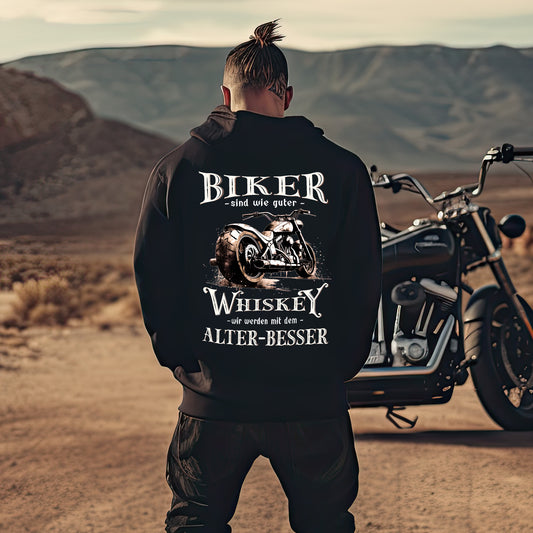 Ein Mann steht vor seinem Motorrad mit einem Biker Hoodie mit einem vintage Aufdruck, Biker sind wie gute Whiskey - wir werden mit dem Alter besser mit Back Print in schwarz. 