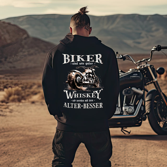 Ein Mann steht vor seinem Motorrad mit einem Biker Hoodie mit einem vintage Aufdruck, Biker sind wie gute Whiskey - wir werden mit dem Alter besser mit Back Print in schwarz. 