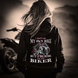 Eine Motorradfahrerin mit einer Reißverschluss-Jacke von Wingbikers mit dem Aufdruck, I Don't Ride My Own Bike, But I Do Ride My Own Biker, in schwarz.