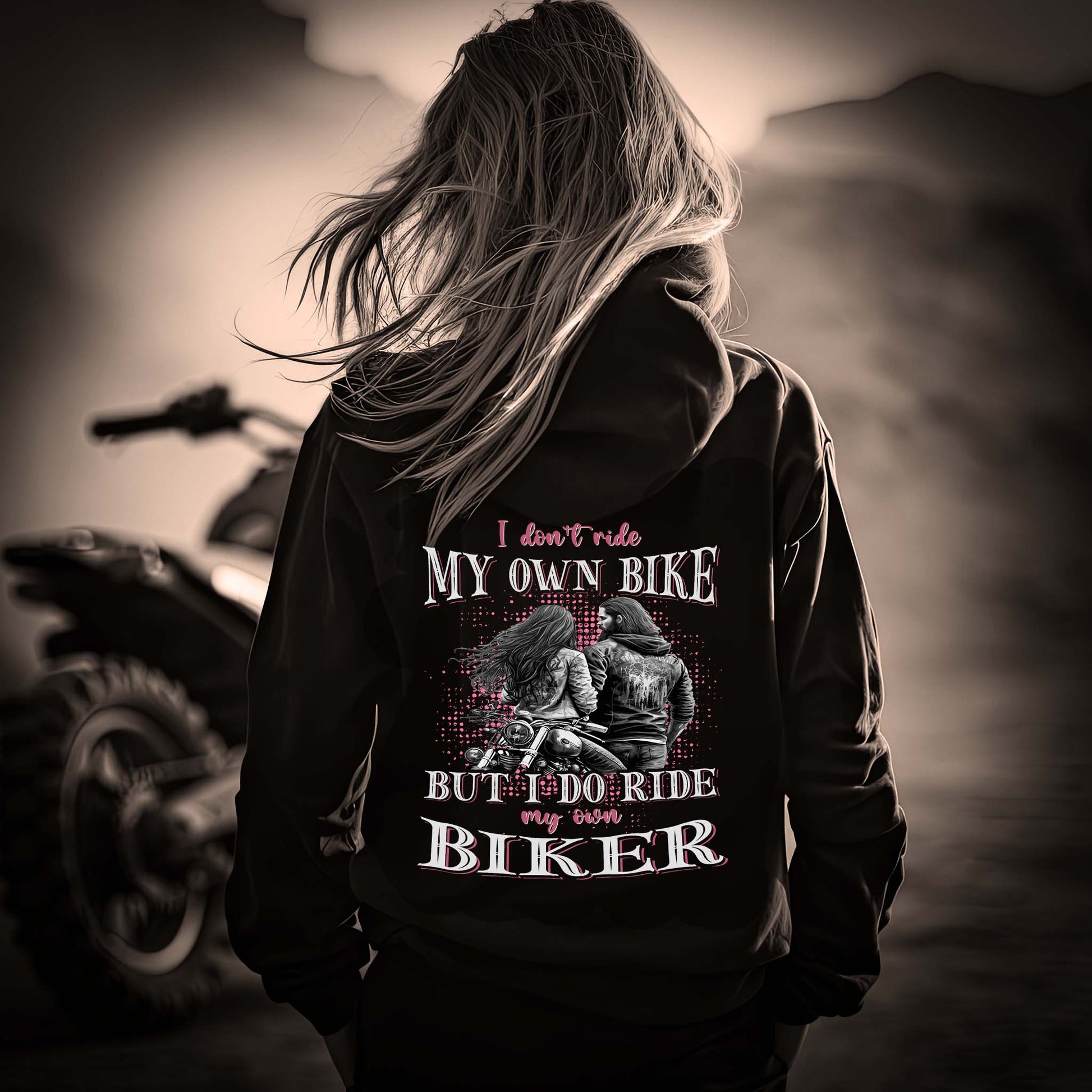 Eine Motorradfahrerin mit einer Reißverschluss-Jacke von Wingbikers mit dem Aufdruck, I Don't Ride My Own Bike, But I Do Ride My Own Biker, in schwarz.